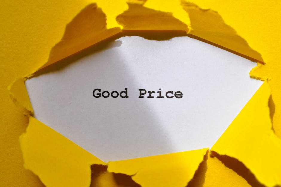 A close-up of a torn yellow paper surface revealing a white inner layer with the words 'Good Price' printed in black. The torn edges are jagged and irregular, showing layers of cardboard or thick paper. This image captures the act of tearing open a package or cardboard box, symbolising affordable or transparent pricing in the context of house removals or moving services. The background and surrounding area are primarily yellow, emphasizing the focus on the message. The visual suggests a connection to packing materials or packaging processes involved in a home relocation, with a subtle hint towards transparent service pricing offered by Pimlico Removals, evident from the professional and clear presentation.